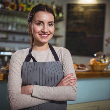 Portrait of smiling waitress standing at counter in cafe
